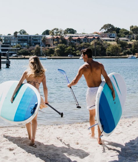 Two hotel guests walk towards the Swan River banks with their paddle boards Image
