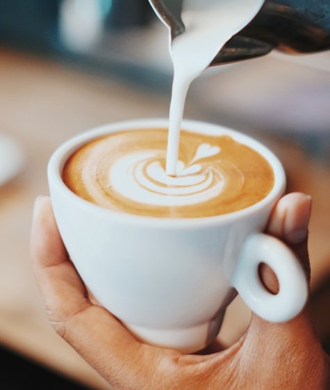A barista pours frothed milk into a coffee cup Image