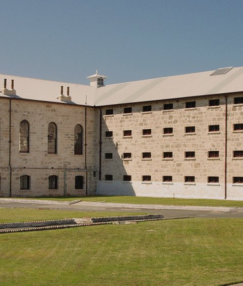 The front of Fremantle Prison, a large old convict-era building with a green lawn Image