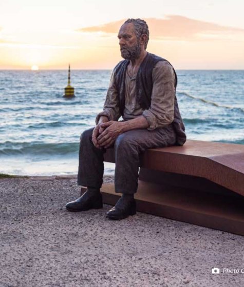 Sculpture of an old man sitting on a bench on the beach Image